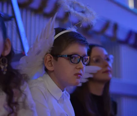 14. Uczeń ubrany w białą koszulę, ma skrzydła na plecach i aureolę na głowie