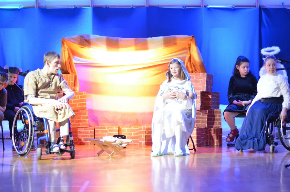 11. Przy szopce siedzą uczniowie grający w Jasełkach. Jest Józef, Maryja trzymająca na kolanach małego Jezusa, Anioły, krowa i osioł