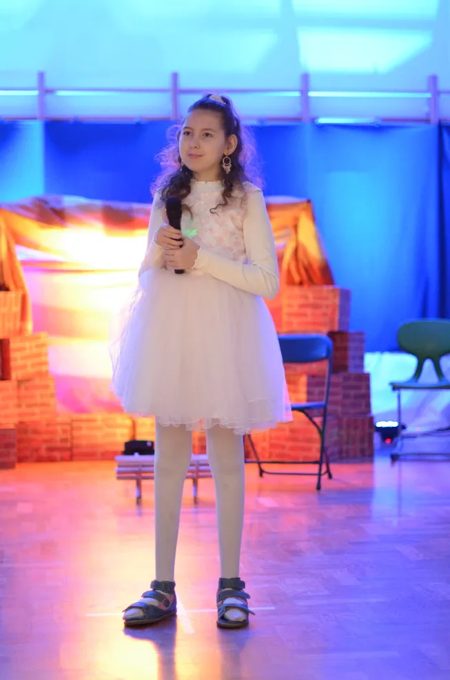 2. Uczennica ubrana w białą sukienkę trzyma mikrofon i śpiewa kolędę