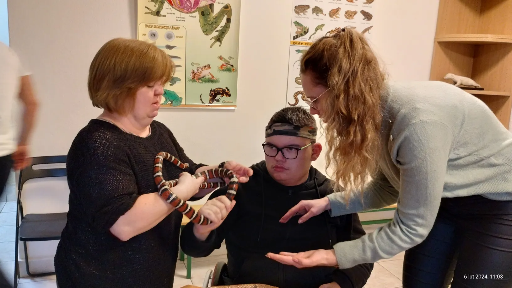 Uczeń trzyma na rękach węża. Wychowawca i opiekun pomagają mu.