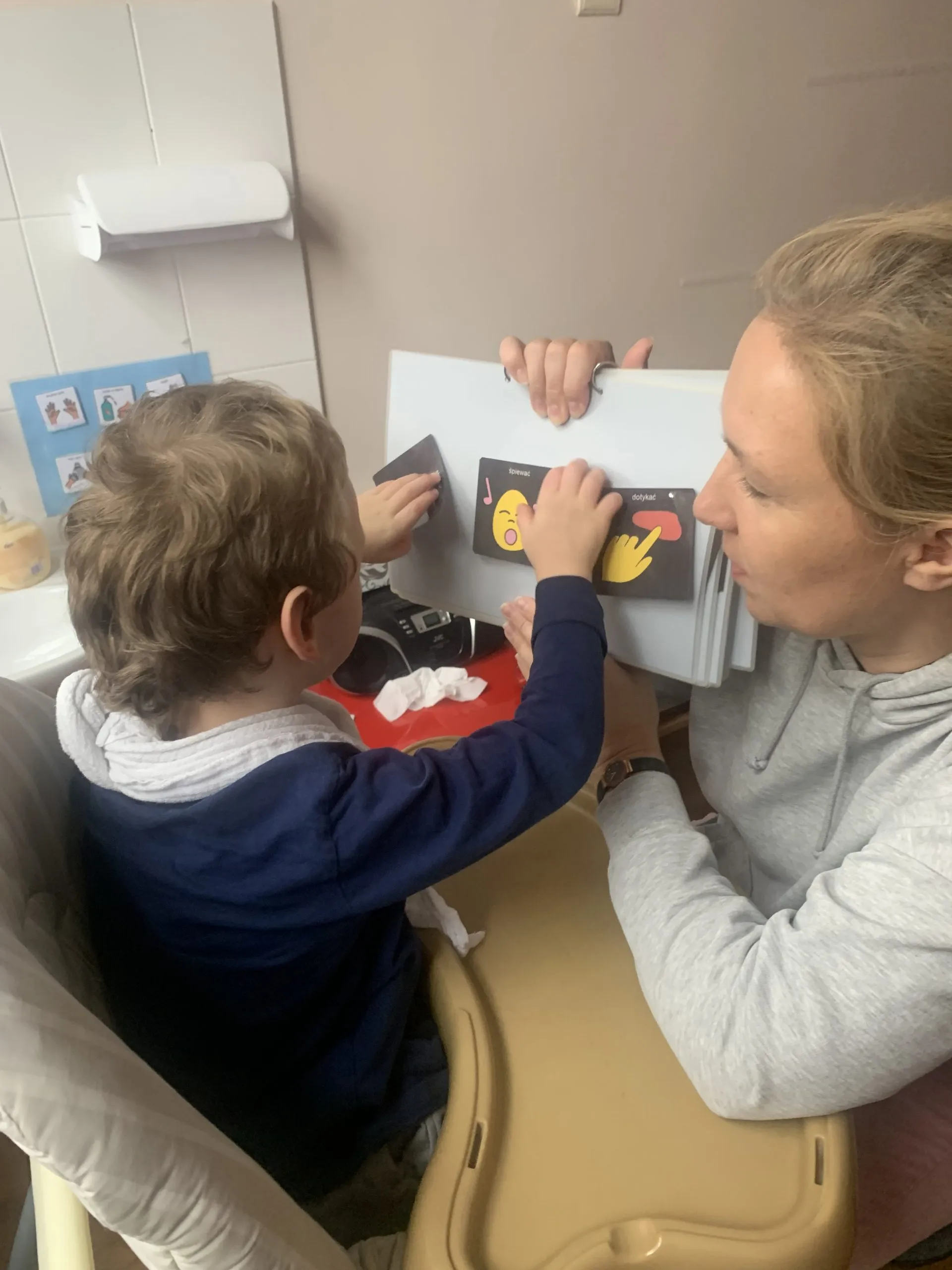 Chłopiec dokonuje wyboru kolejnej czynności na kontrastowych symbolach w indywidualnej książce do komunikacji.