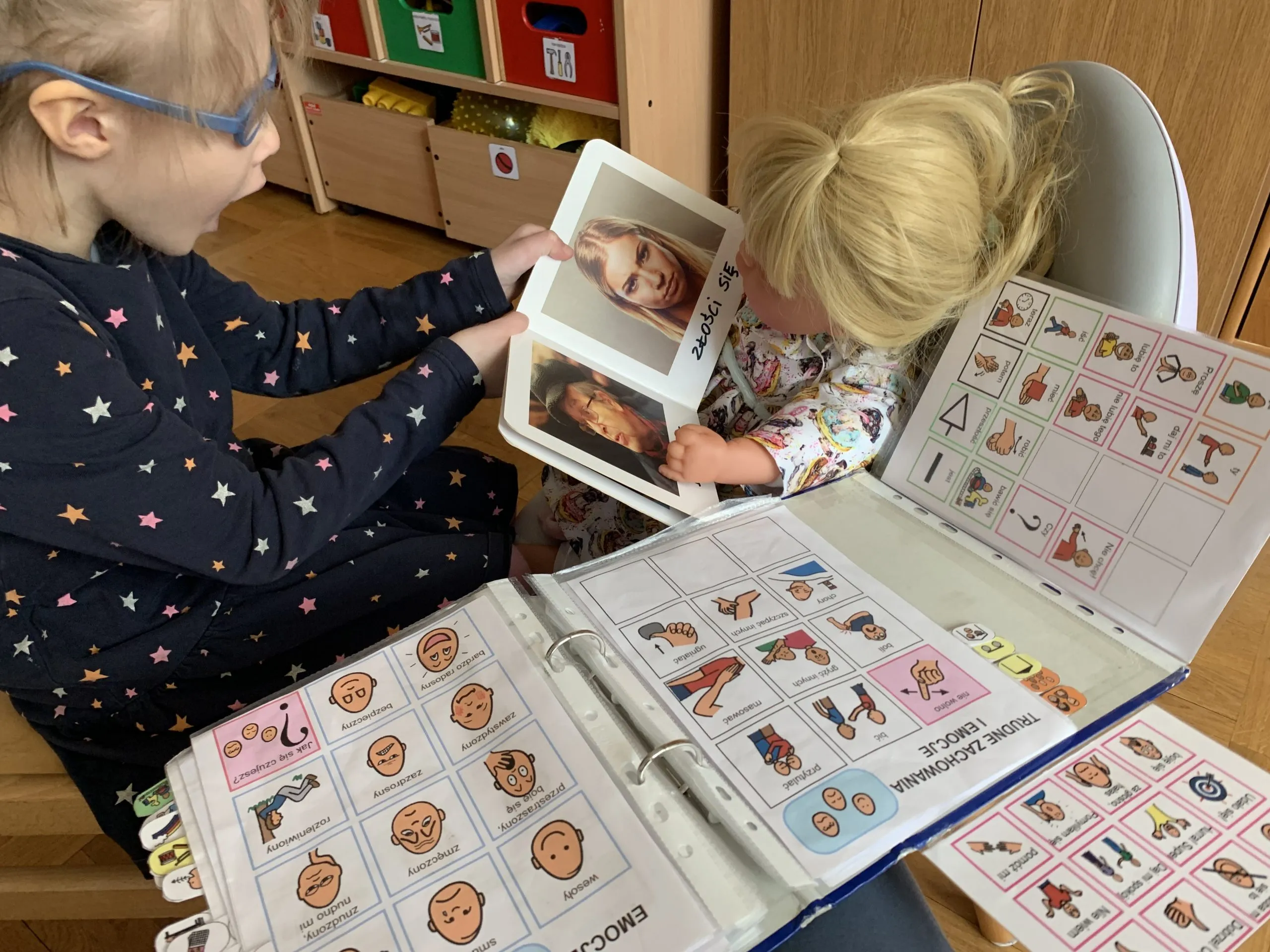 Dziewczynka czyta książkę lalce wykorzystując indywidualną książkę do komunikacji oraz komunikację werbalną.