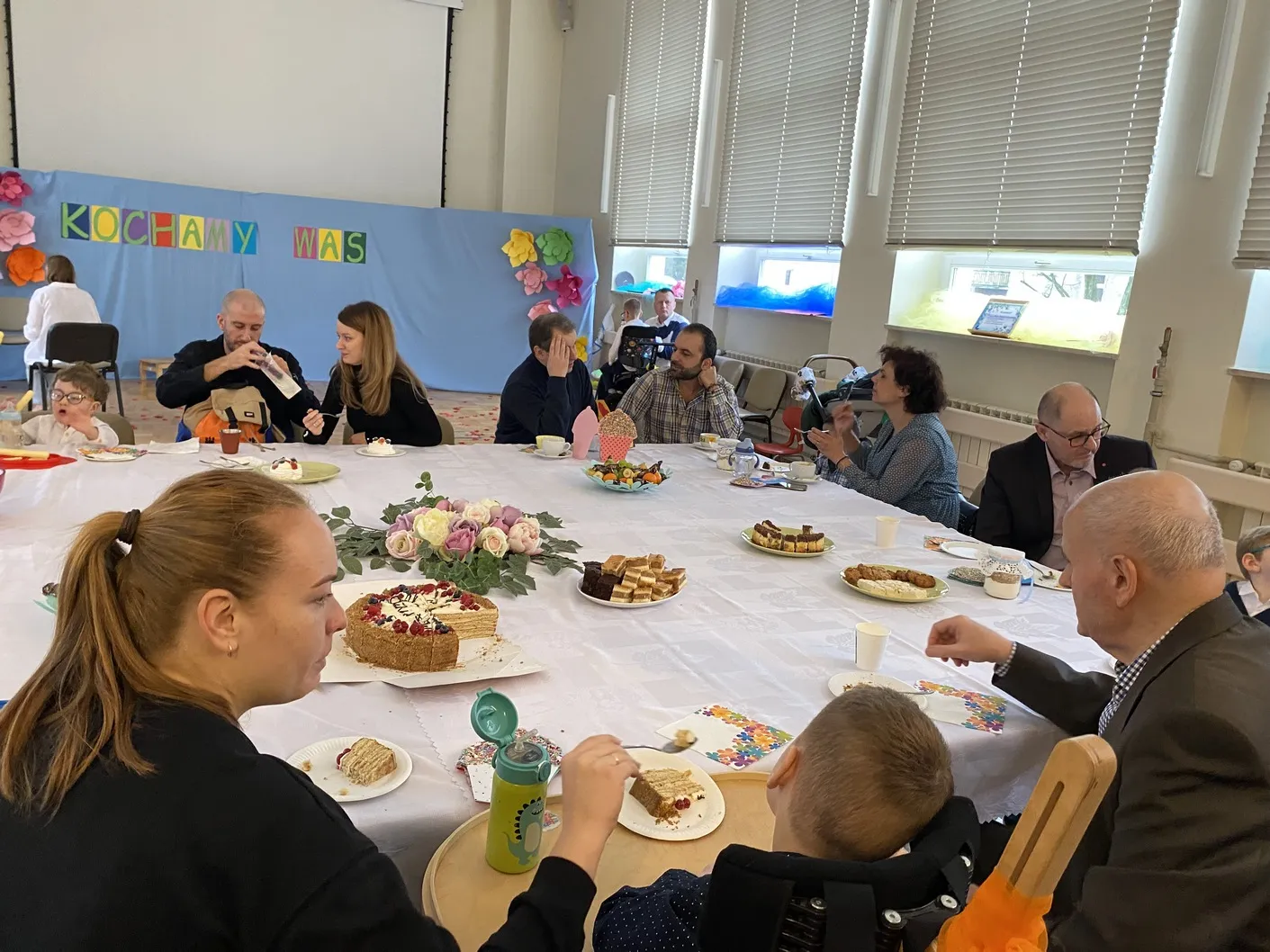 Dziadkowie oraz rodzice przedszkolaków siedzą przy stole – rozmawiają, piją kawę, jedzą ciasto