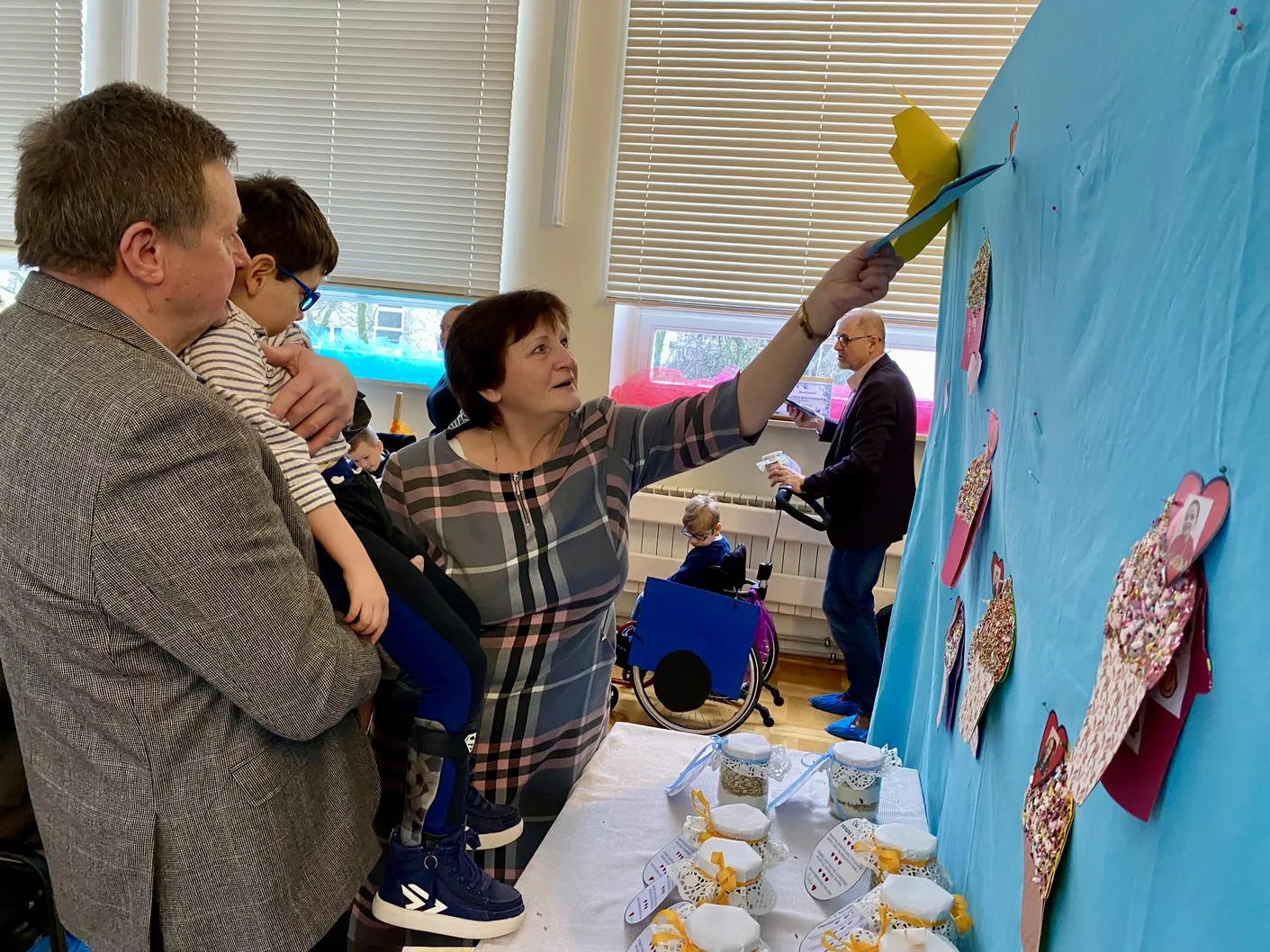 Dziadkowie odszukują na tablicy laurkę wykonaną przez wnuka